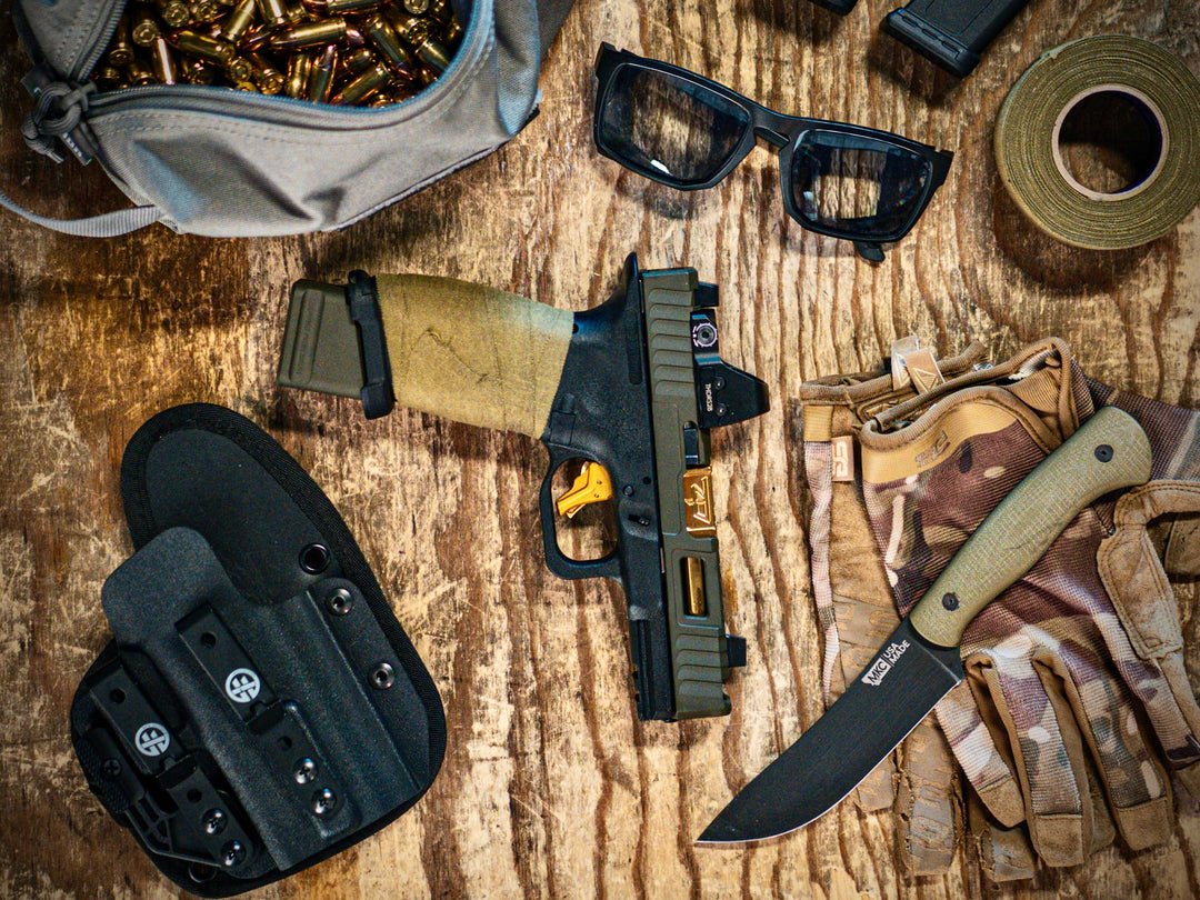 Black OMNICARRY IWB holster on a table with pistol, magazine, and everyday carry gear, showing a secure multi-fit holster option for beginners.