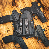 OMNICARRY IWB holster surrounded by multiple compact pistols on a wooden surface, showing multi-fit compatibility for 300+ handgun models.